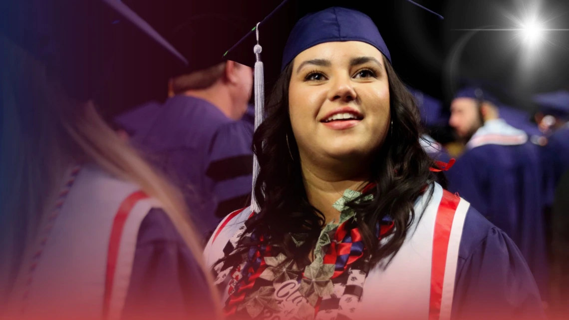 Graduating student in cap and gown smiling during the University of Arizona College of Education, other students in the background