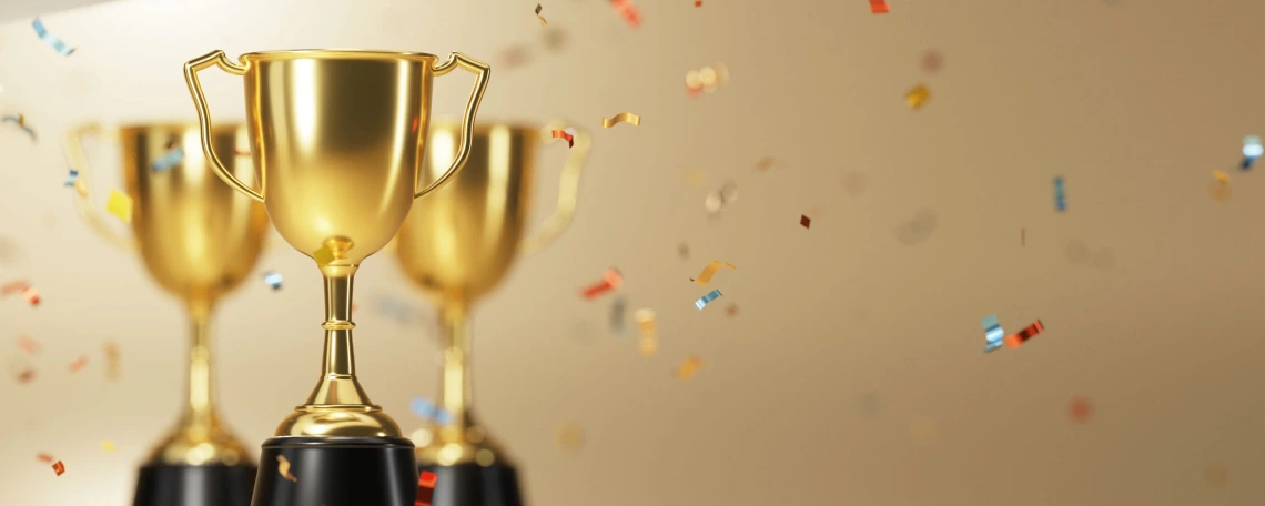 Golden trophies with black bases surrounded by colorful confetti falling in celebration against a soft, neutral background.