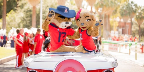 wilbur and wilma sitting on a car during homecoming parade waving