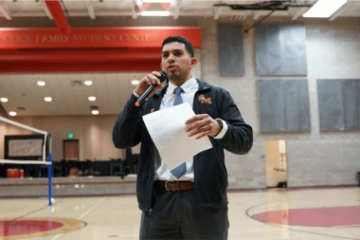 Ricardo_Dominguez holding a microphone and paper in hand speaking in auditorium setting