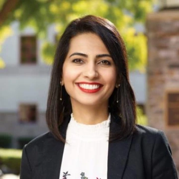 Saeideh Heshmati headshot, medium length dark brown hair, wearing a black blazer over a white blouse, smiling under a sunny sky