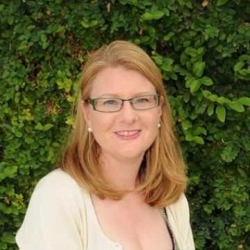 jessica summers headshot, wearing eyeglasses, blonde medium length hair, with greenery in the background