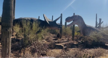 two large dinosaur structures in a desert landscape under a sunny sky