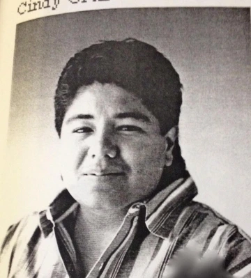 Black-and-white portrait of Cindy Cruz from a yearbook or archival publication. She has short, dark hair and is wearing a striped shirt with the collar open. Expression is calm and confident.