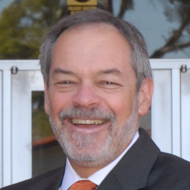 ron marx headshot, wearing a suit and tie, salt pepper hair, standing outside the college of education building