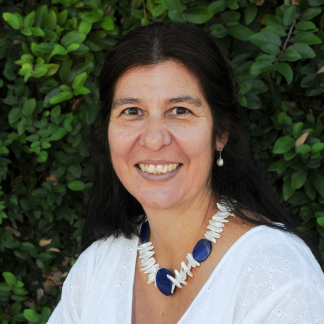 sara chavarria headshot, wearing a white blouse with greenery in the background