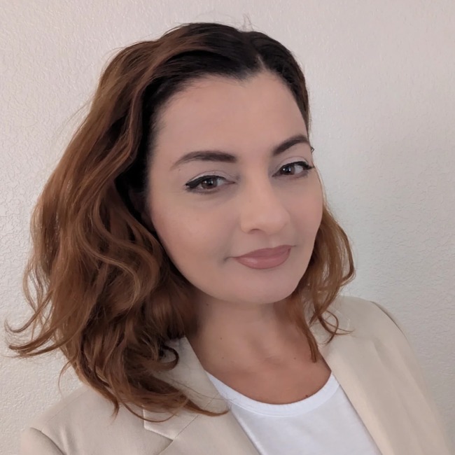 Portrait of Diba Fallah wearing a light beige blazer and white shirt, standing against a neutral wall background.